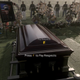 People attend a funeral for a fallen service member while a dialogue prompt asks the player to pay their respects.